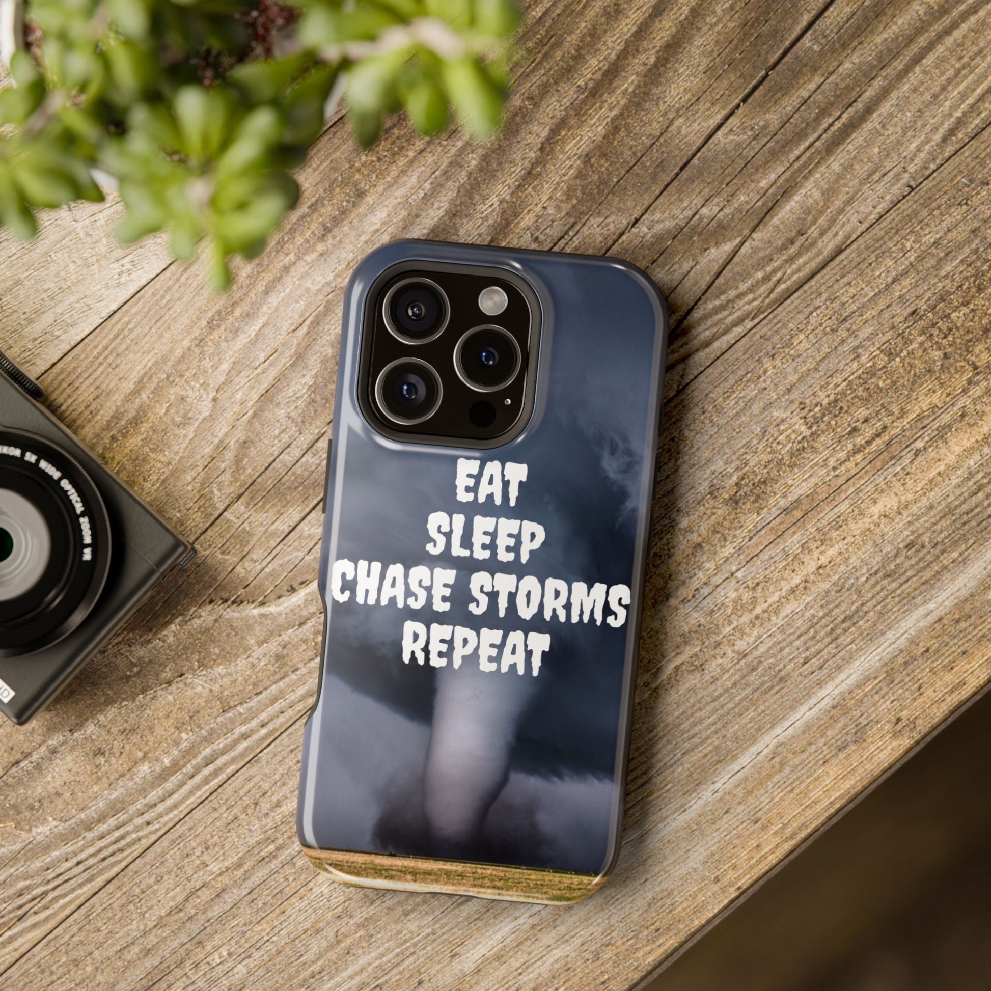 Impact-resistant phone case with "Eat Sleep Chase Storms Repeat" design on a wooden surface.
